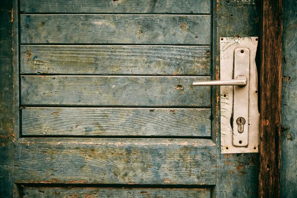 Worn metal door lock, slightly twisted, on an aged door.